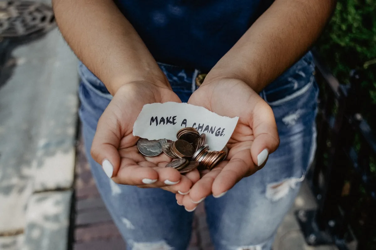 Hands holding coins with a note reading “Make a change”